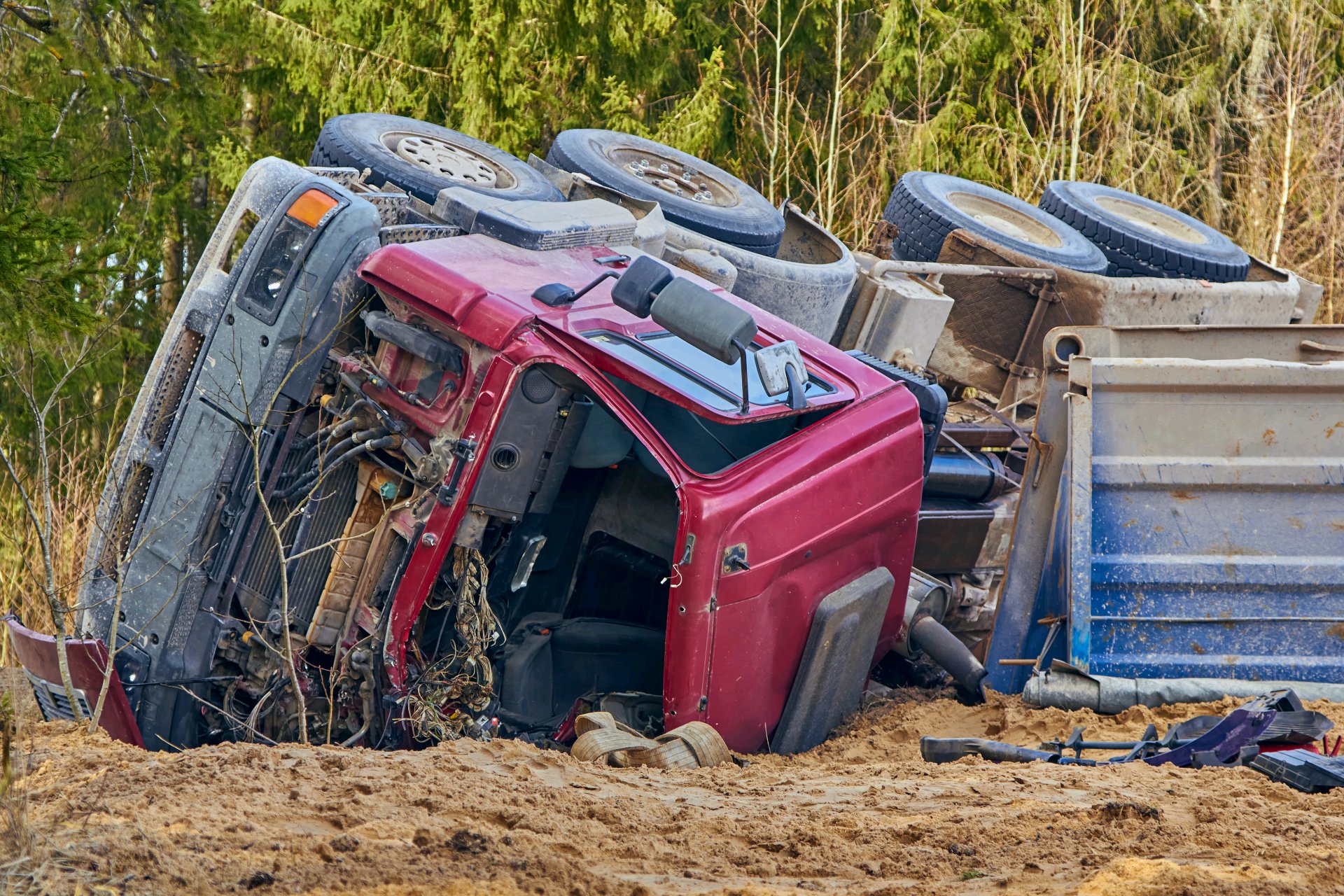 Overturned commercial truck beside a wooded roadside after a collision.