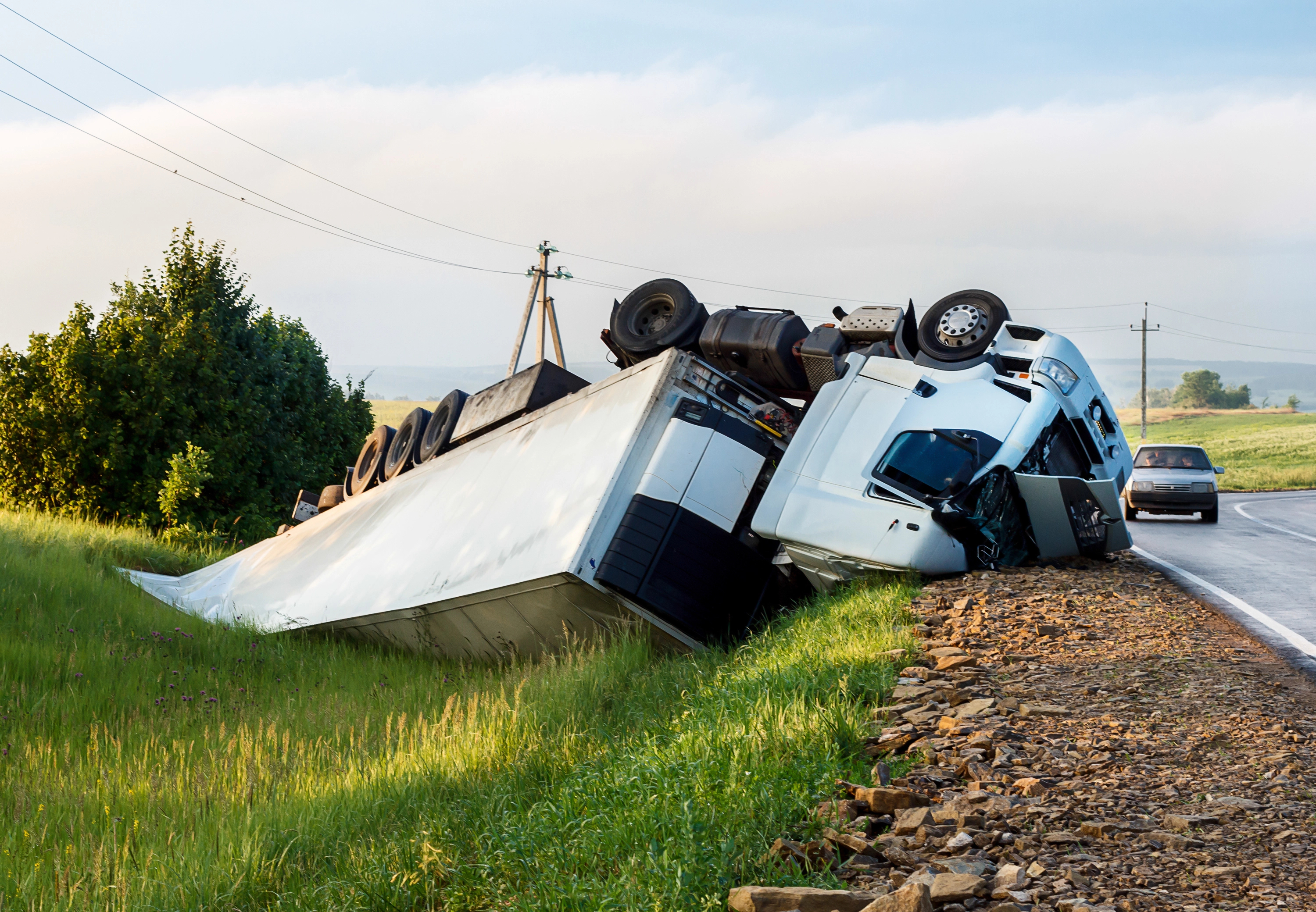 Overturned white semi-truck beside a rural roadway after a crash.