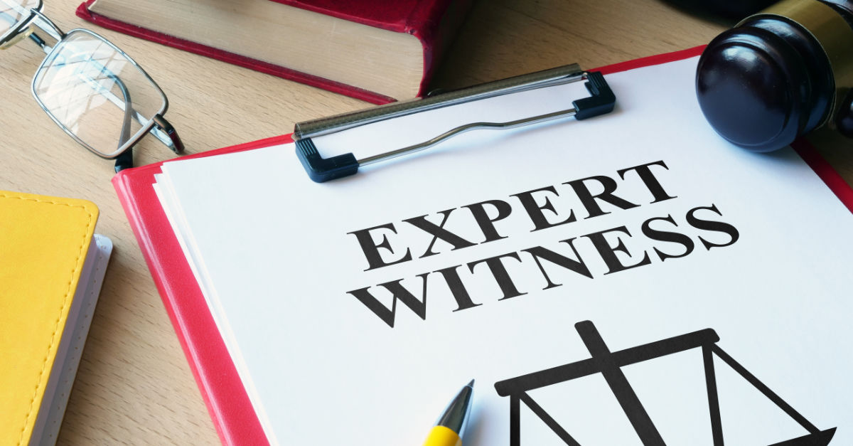 Expert witness text on paper attached to clipboard on desk with other items